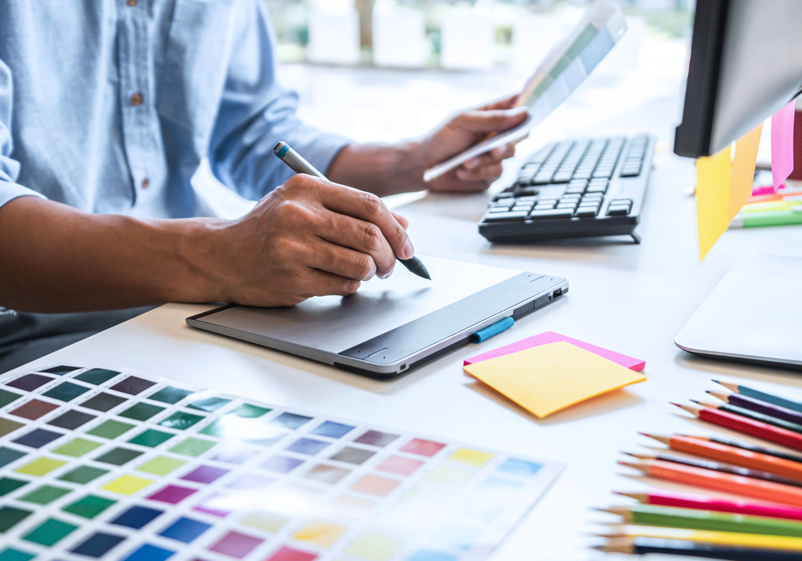 Two colleague creative graphic designer working on color selection and color swatches, drawing on graphics tablet at workplace with work tools and accessories.