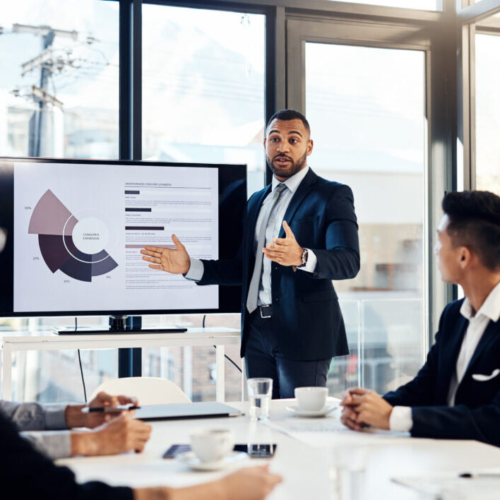 Workshop, meeting and finance with a business man talking to his team in the office boardroom. Training, presentation and education with a male coach teaching staff using a graph display at work.